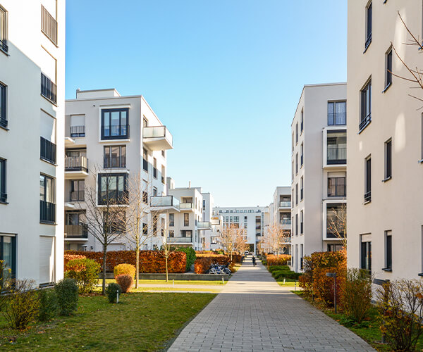 Eine moderne Wohnanlage mit mehreren weißen Mehrfamilienhäusern, gepflegten Grünflächen und einem gepflasterten Gehweg, der durch die Anlage führt
